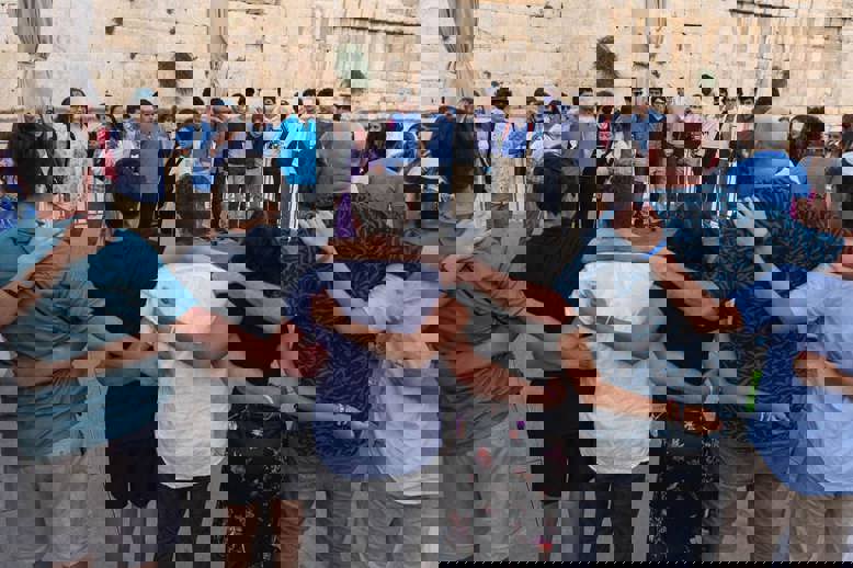 קהל מגוון של אנשים חוגג בקונצרט, מרימים את ידיהם ומריעים.